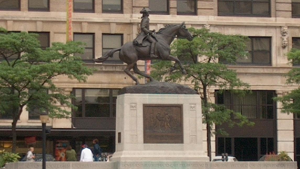A bronze statue of a man on a horse in front of a modern building.