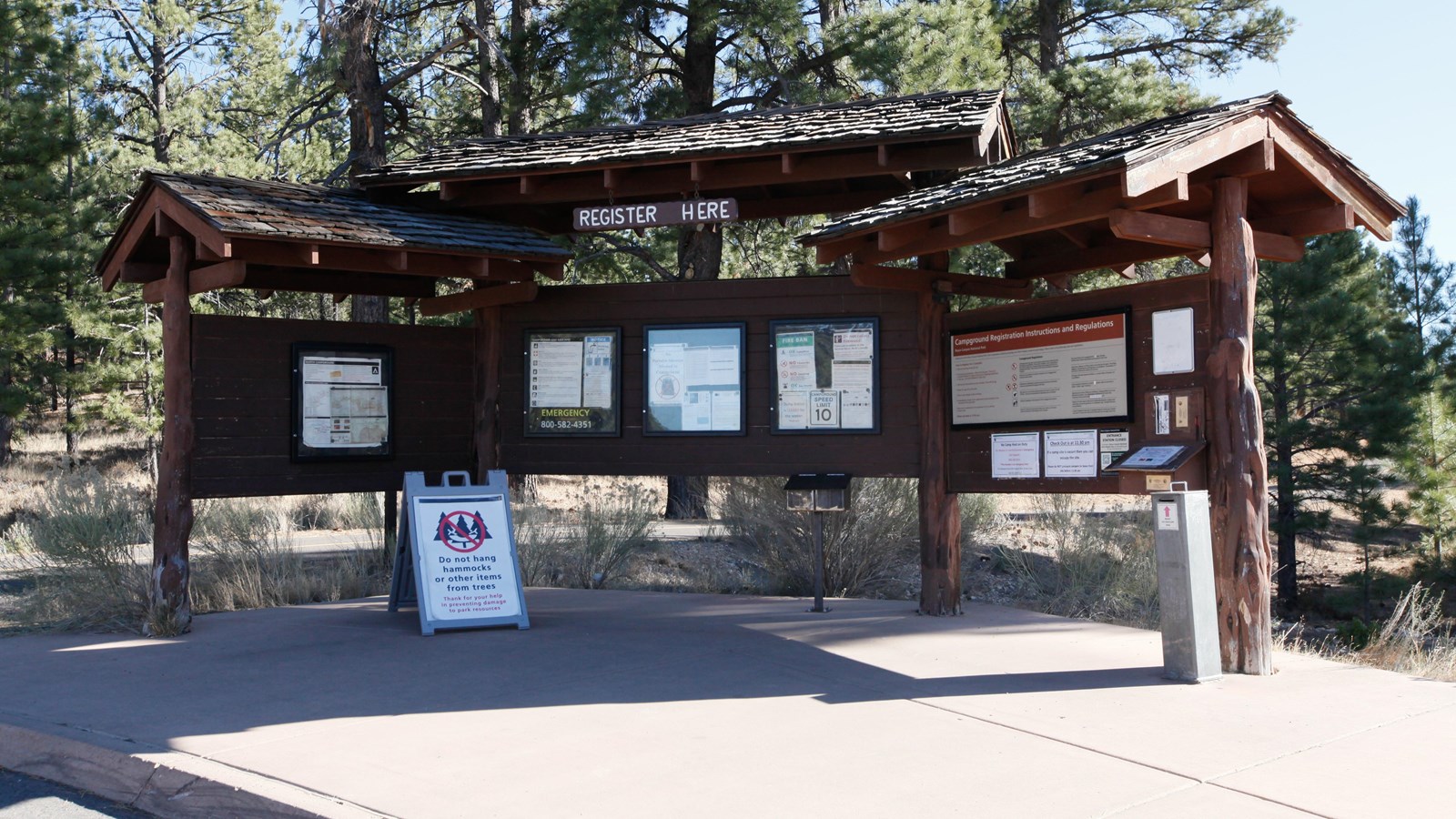 A brown wooden kiosk with multiple information panels sits below green shingled awnings