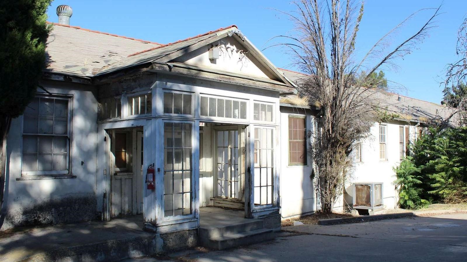 A dilapidated white building with a porch partially enclosed with windows.