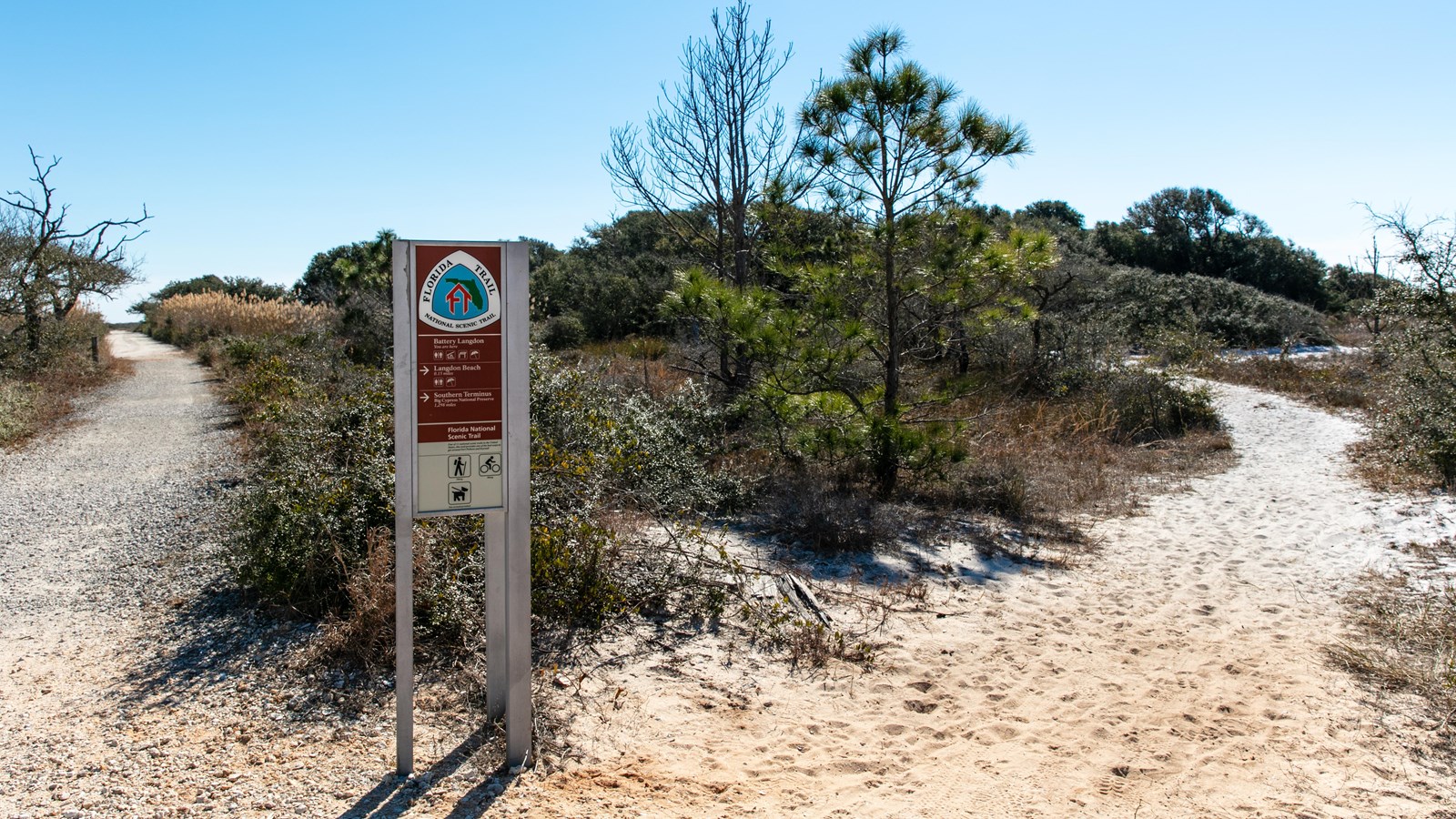 A sign for the Florida National Scenic Trail stands in front of an gravel trail and vegetation.