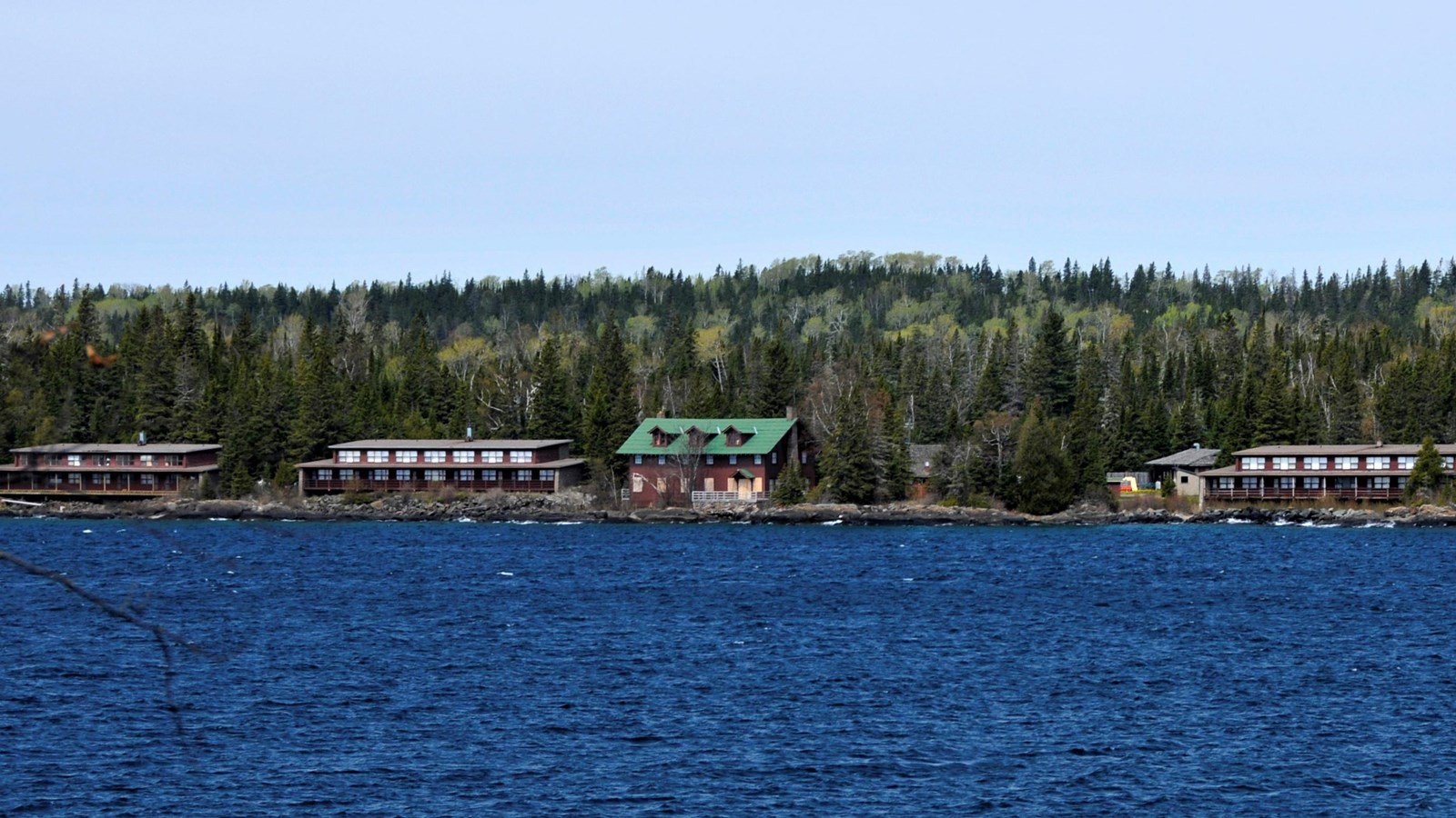 Buildings a part of the Rock Harbor Lodge sit on the shore of Lake Superior with a forest in back.