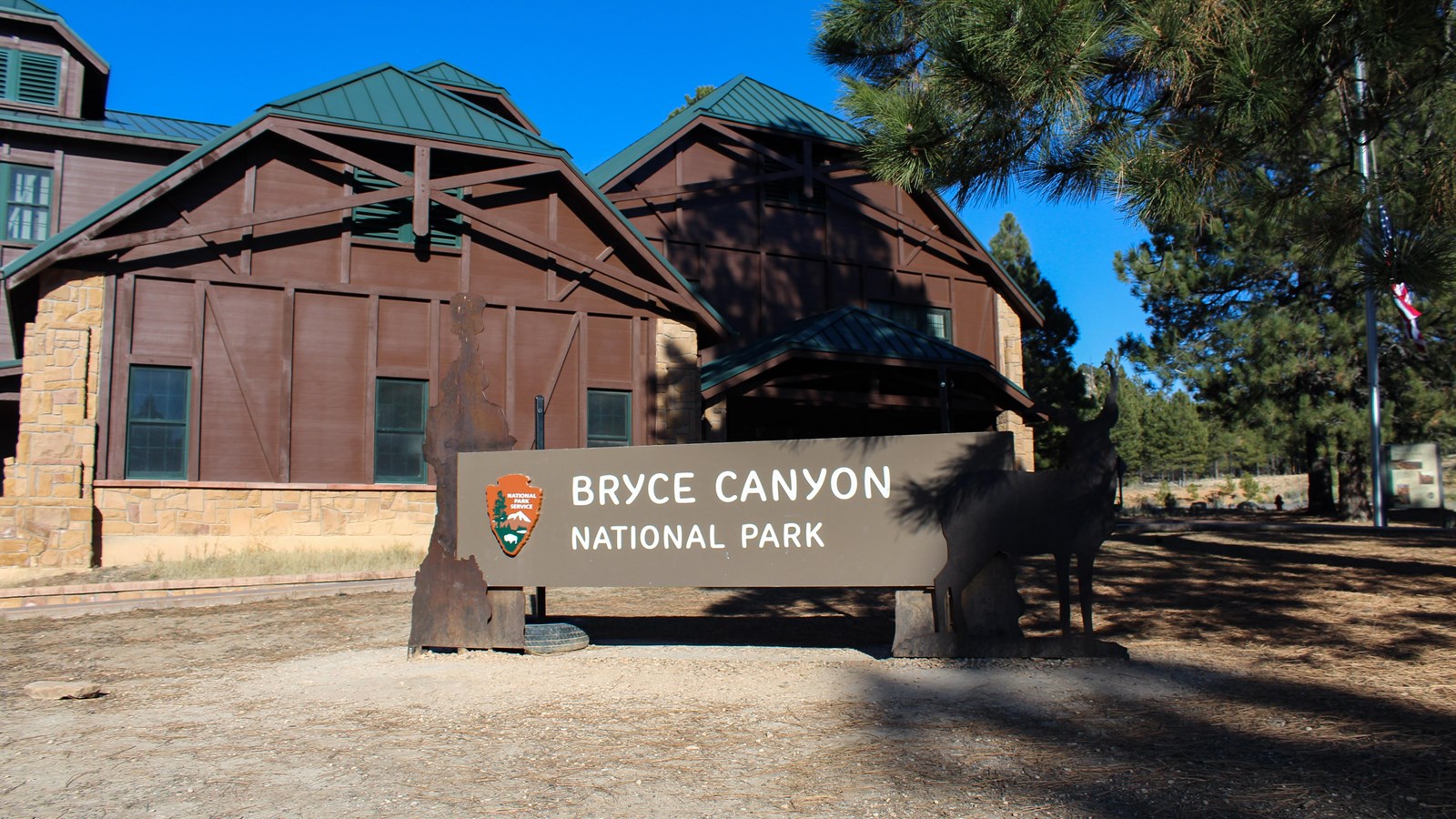 A metal sign reading Bryce Canyon National Park stands in front of a large building with green roof