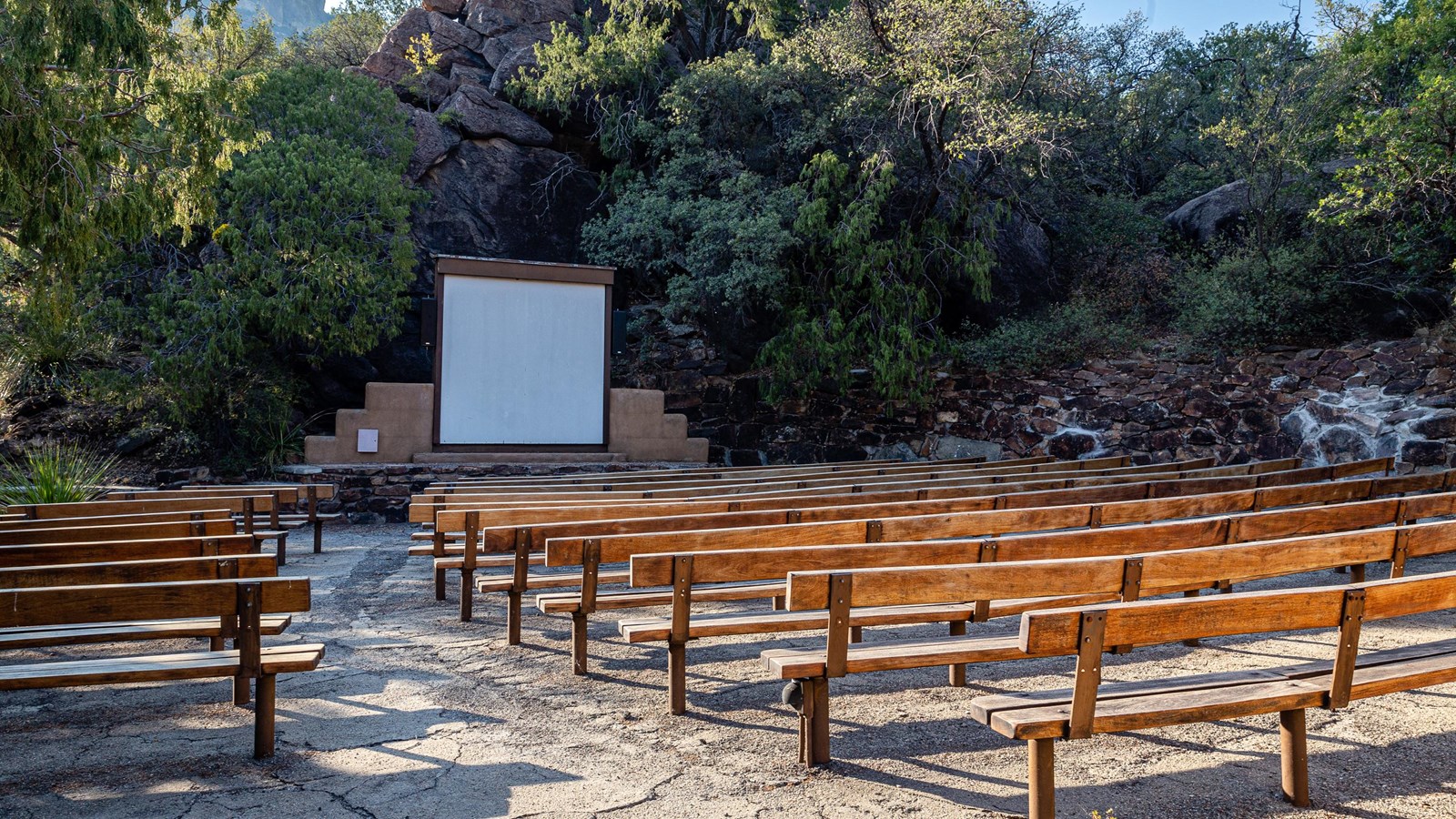 An outdoor screen and small stone stage are surrounded by wooden benches