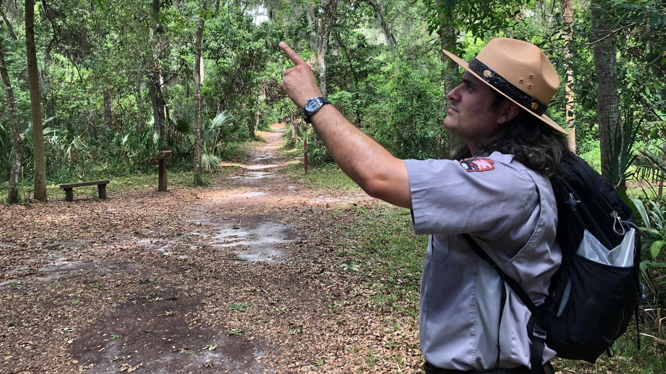a ranger with a backpack in the woods pointing