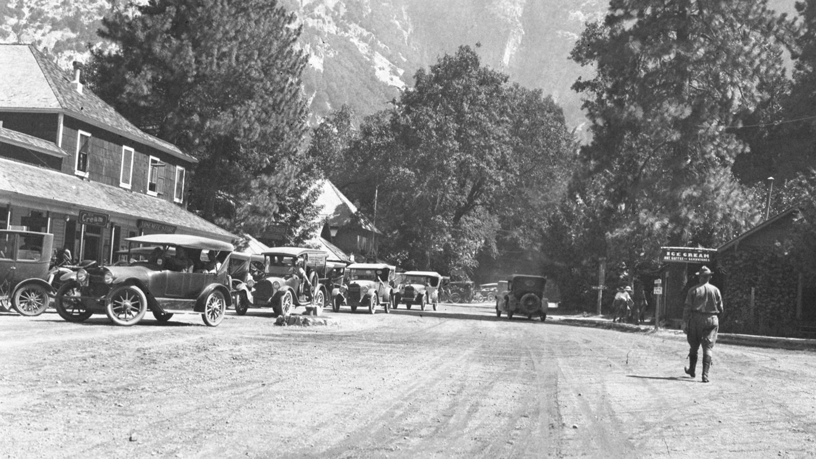 Historic image of cars on a dirt road near old buildings in former Yosemite Village