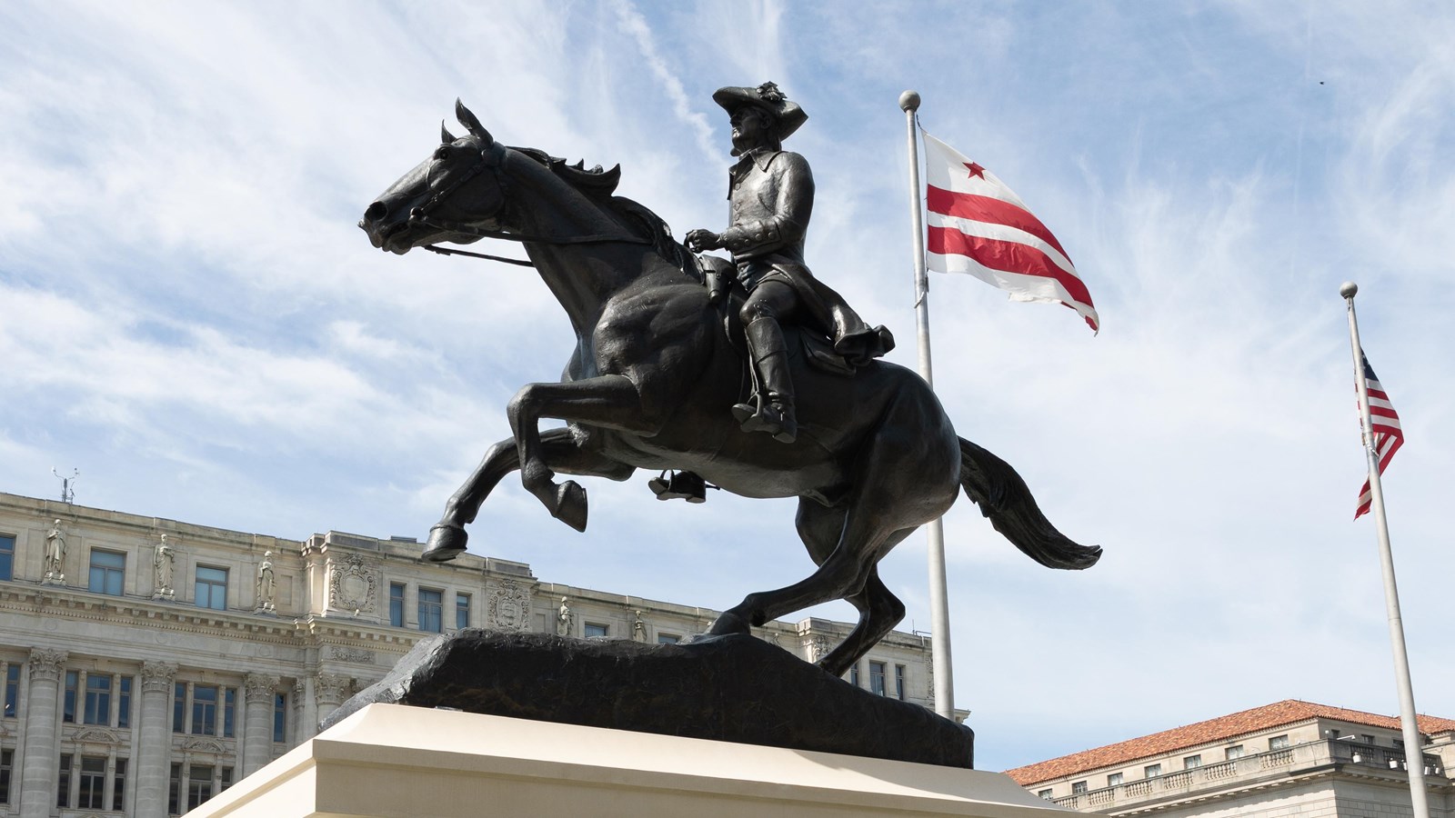 A bronze statue of a man on a galloping horse. The DC flag flutters in the background.