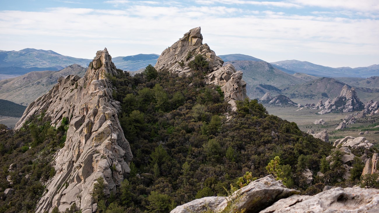 2 prominent granite features jut up in the foreground with a rocky mountainous landscape behind.