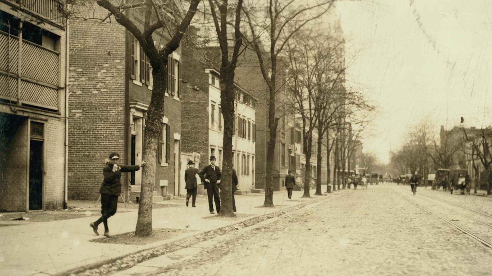 Men dressed in early twentieth century suits stand on a dirt street.
