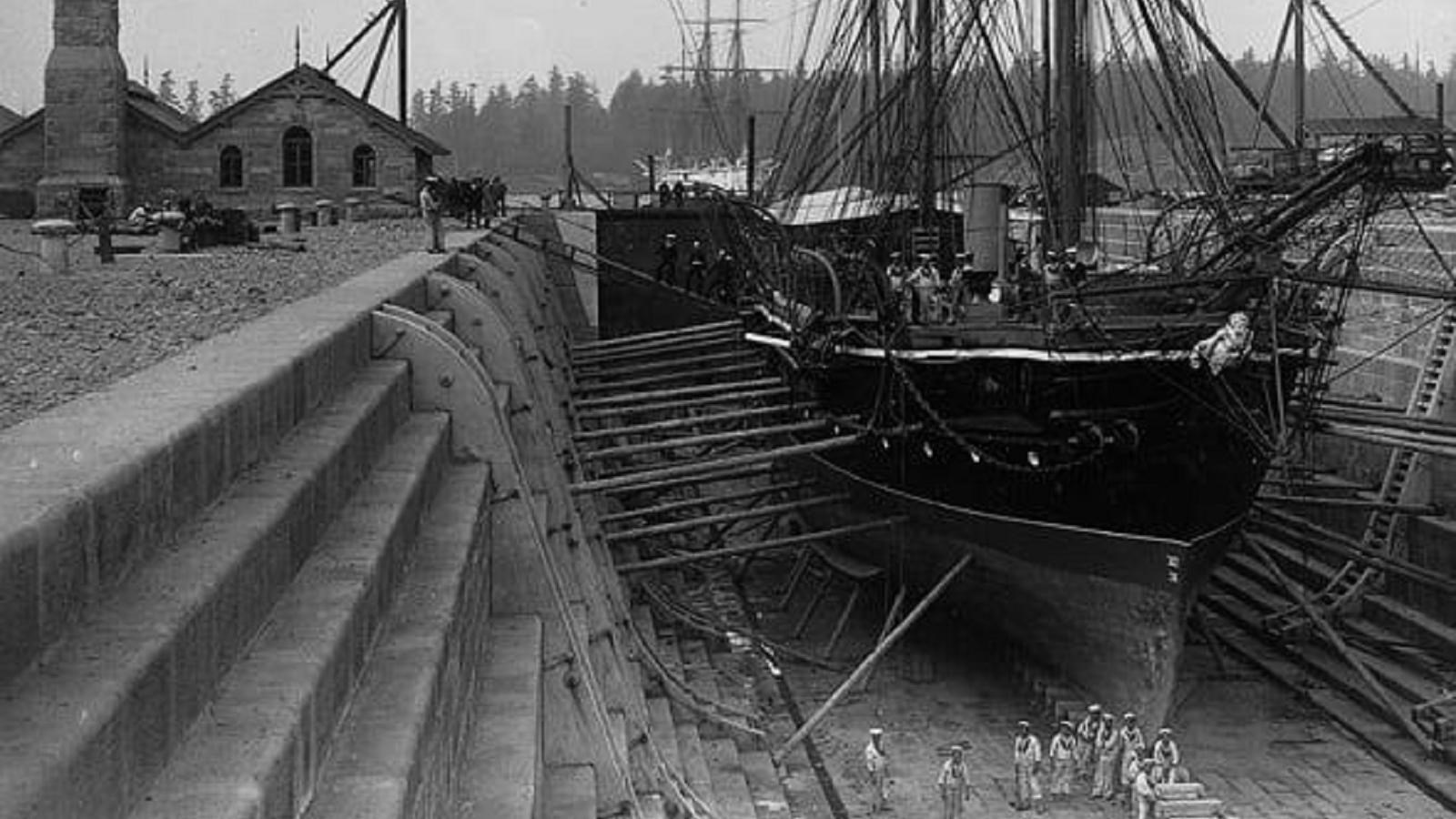 Black and white photograph of a large, three masted ship in a drydock