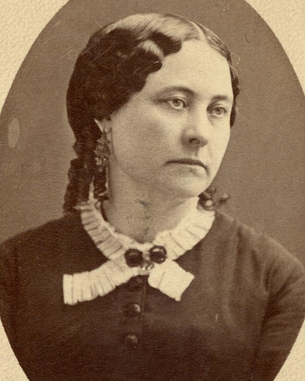 A woman with dark hair and dark colored dress with a lace collar.