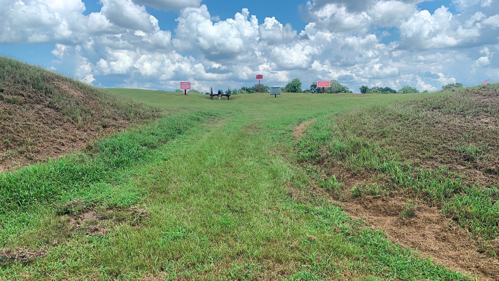 A grassy upward sloping entrance into a square earthen fort called