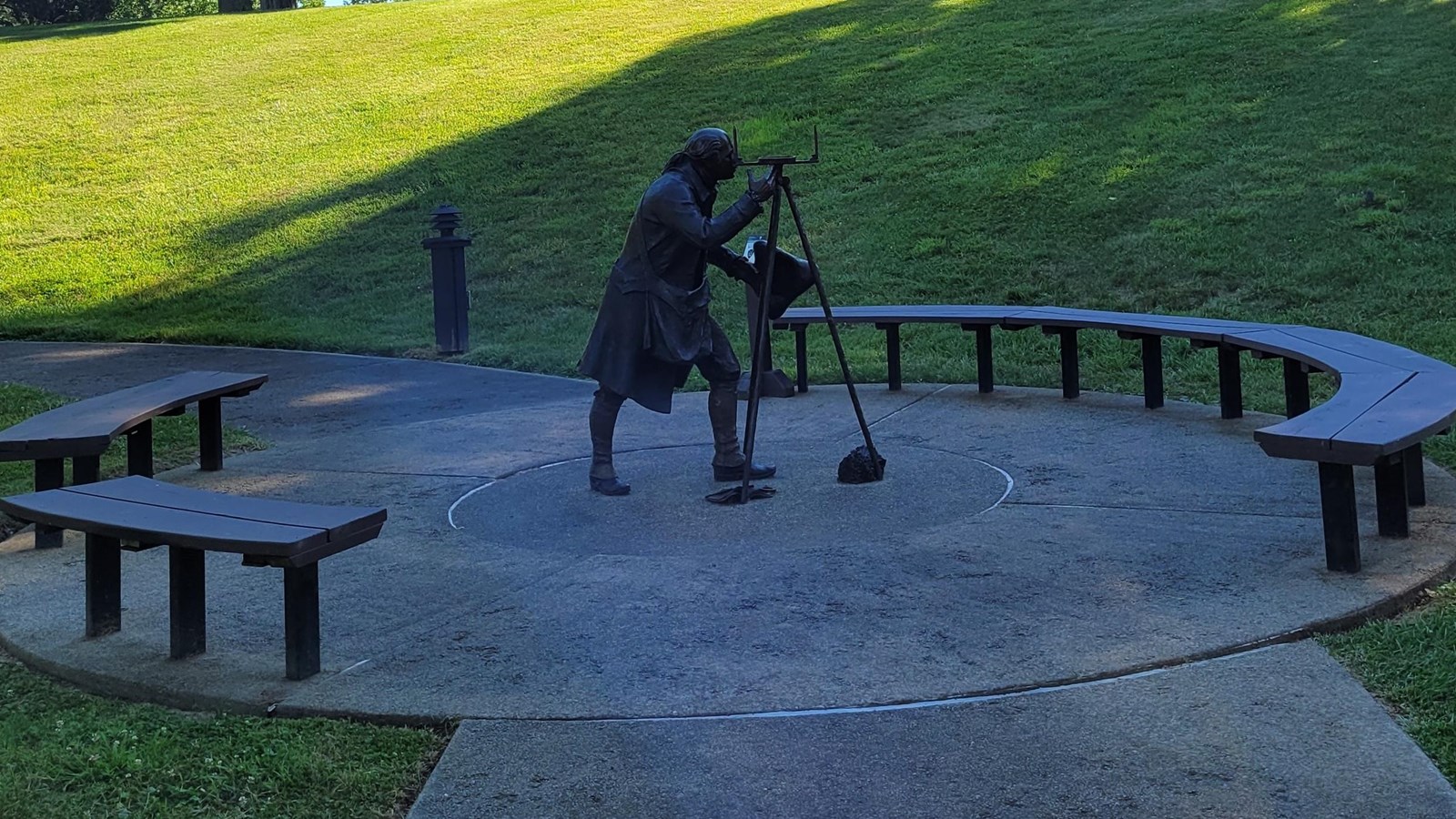 Metal statue of a young balding man with surveying tools looking through an object on a tripod