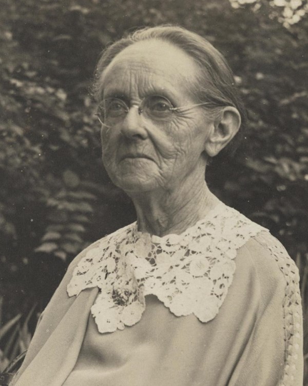 A women wearing glasses in a top with a lace collar. 