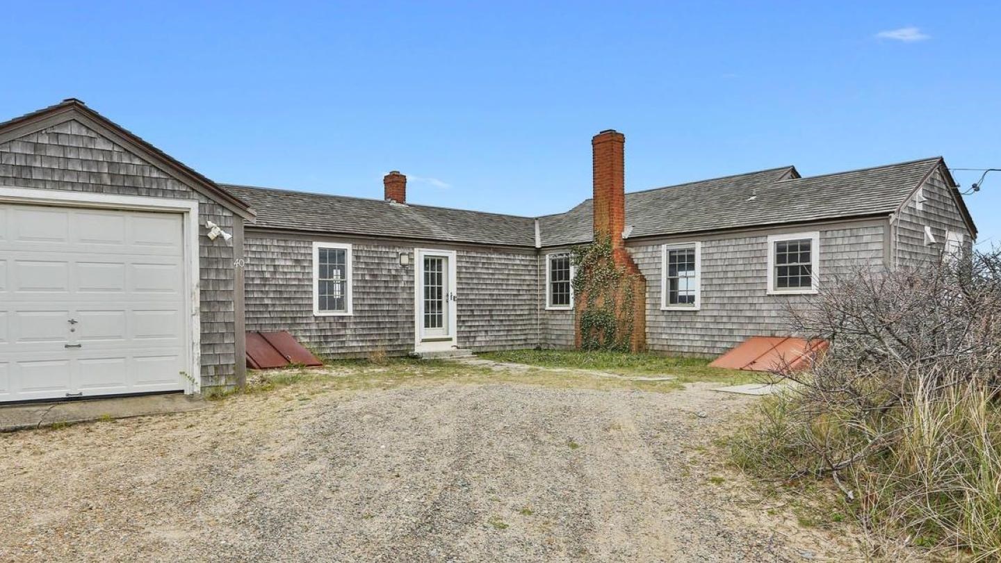 Outside view of the home from the driveway. A one-story home with a garage and chimney.