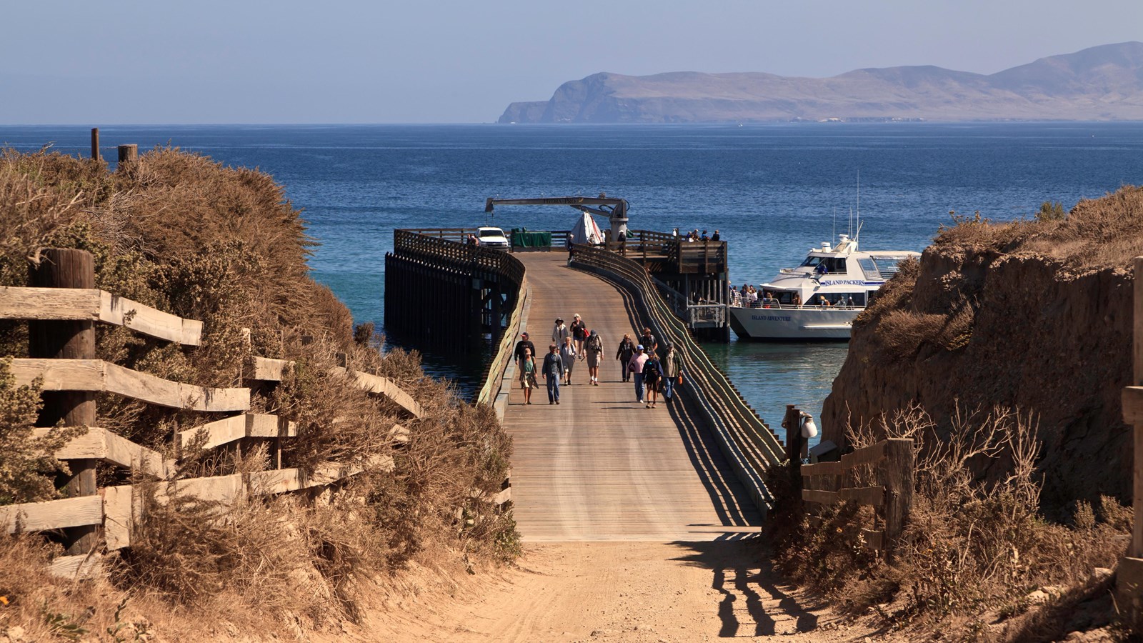 Long wood pier with railings and boat tide up at end. Island on horizon. 