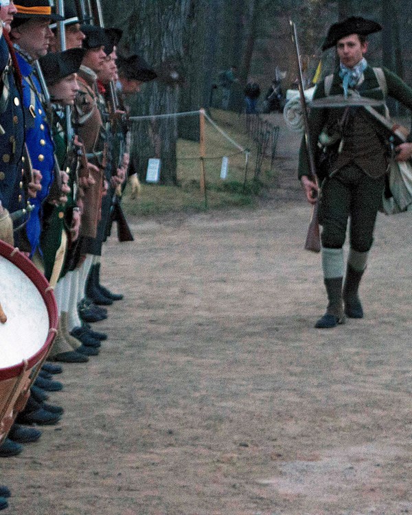 Line of Revolutionary War militia soldiers, including a drummer, stand at attention.