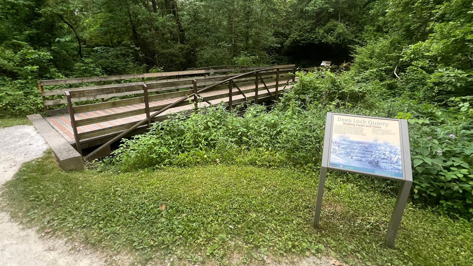 An exhibit panel next to a pedestrian bridge over a plant-filled canal.