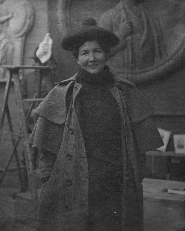 Smiling woman in turtleneck, long unbuttoned coat, and beret standing in sculpture studio