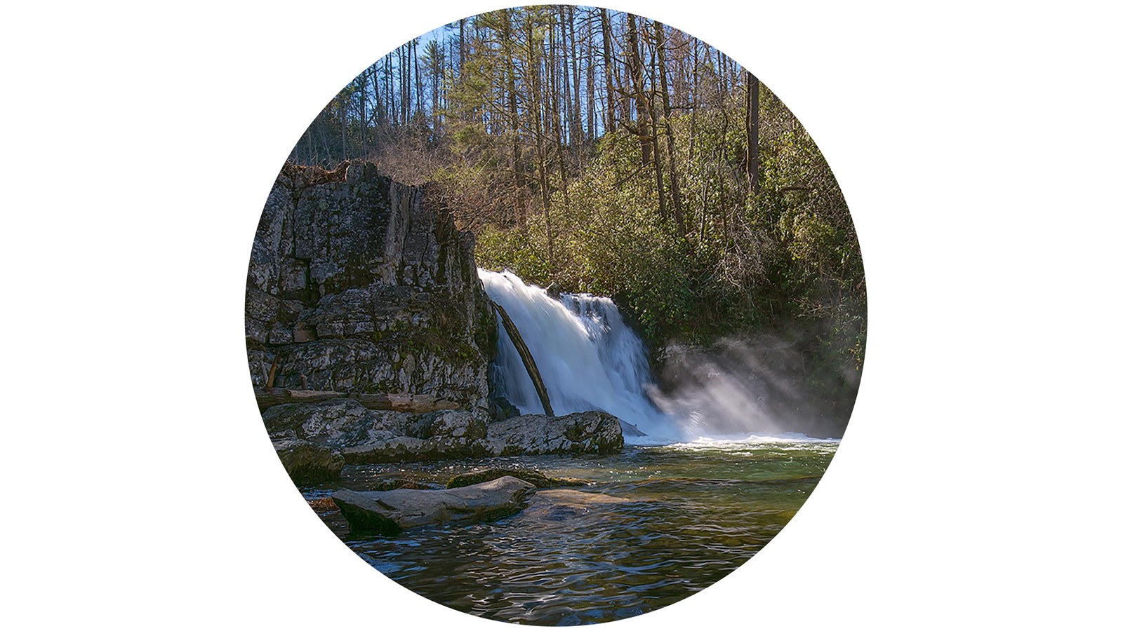 A waterfall flowing into a pool below, with mist around the base. Trees and rocks surround the falls