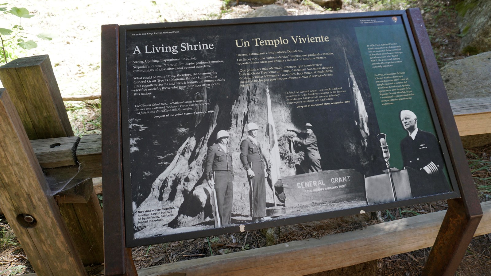 A metal framed sign with images and text on it stands in front of a wooden fence