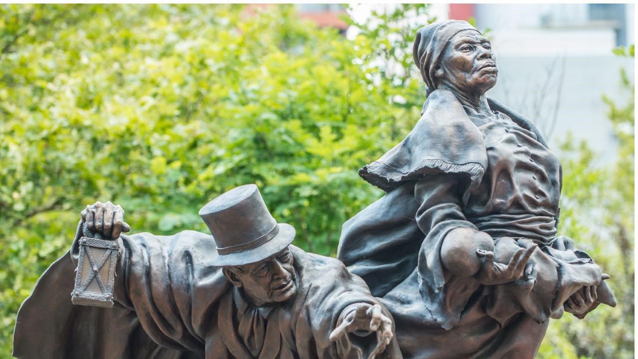 Harriet Tubman hold a baby in her arms as Thomas Garrett, at her side holds a lantern.  