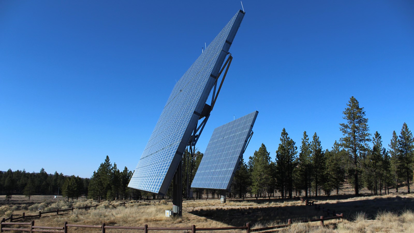 Two solar panels stand in field surrounded by brown wooden fence