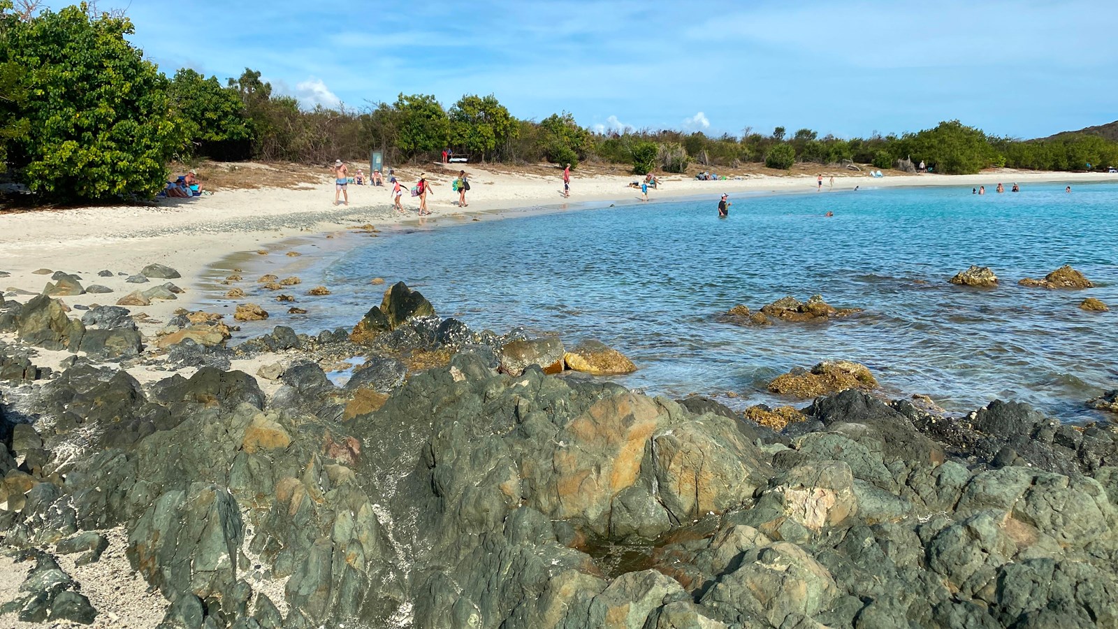 A long white sand beach curves gently around crystal clear turquoise water.