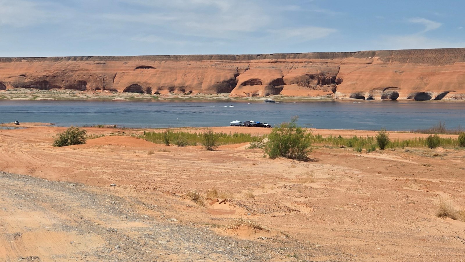 Gravel and sand beach with some people at the water\'s edge under umbrellas.