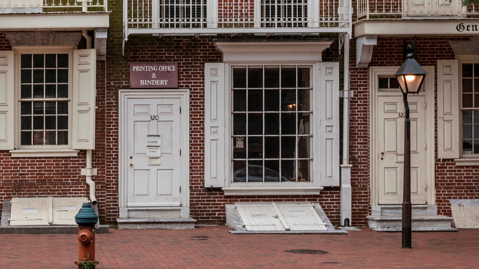 A color photo of a red brick row house with a large multipaned glass window on the first floor