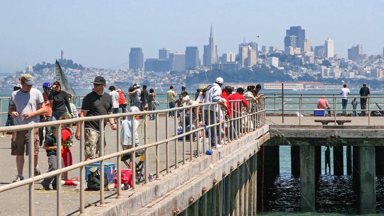 Looking down the length of a fishing pier, scattered with people walking and fishing.