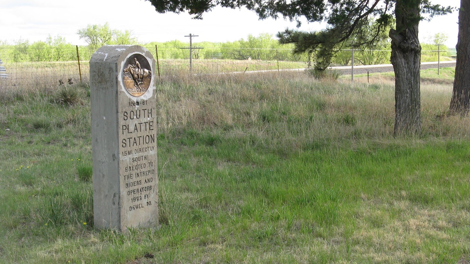 A stone monument sits in the grass next to a tree.