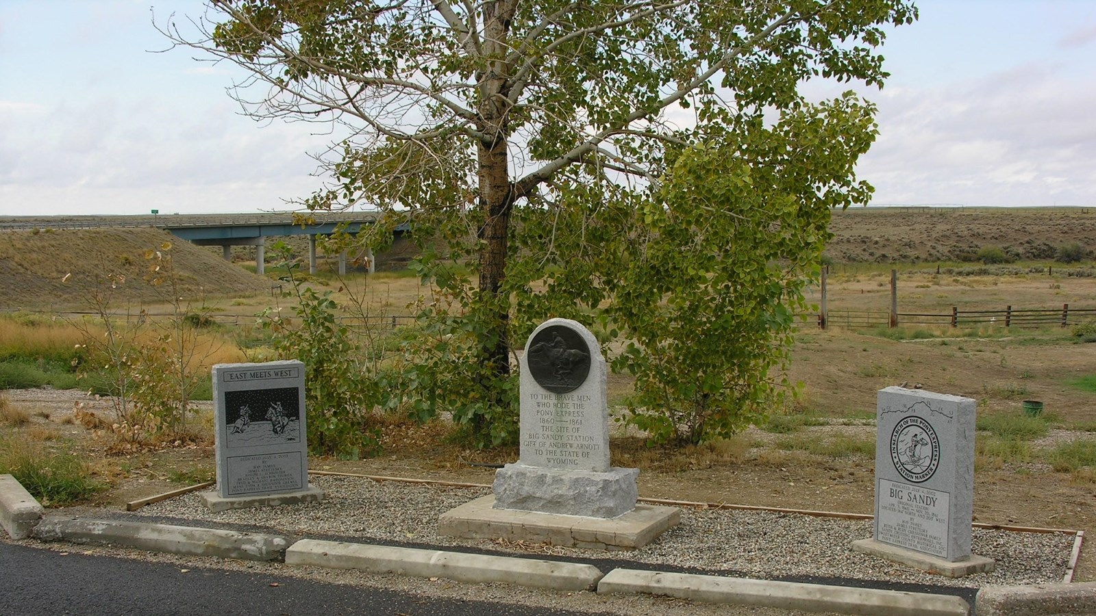 Three stone monuments sit next to a tree alongside a road.