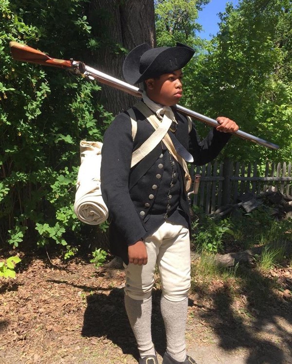 Revolutionary War soldier in black hat and black coat carrying his musket over his shoulder