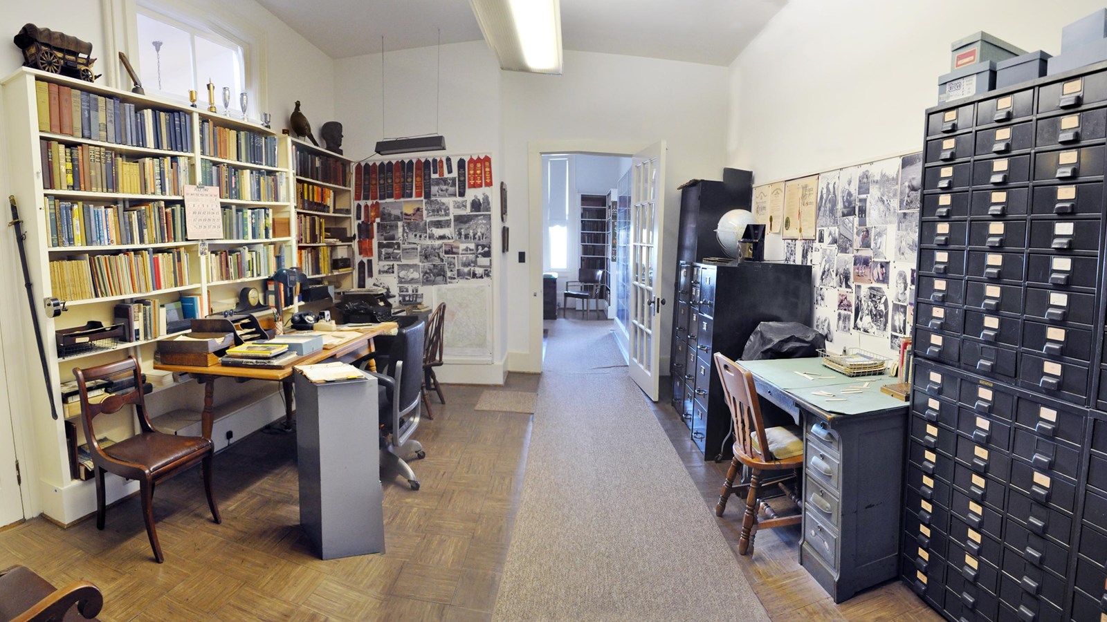 image of office with bookshelves, dark metal filing cabinets and photos pinned to the wall