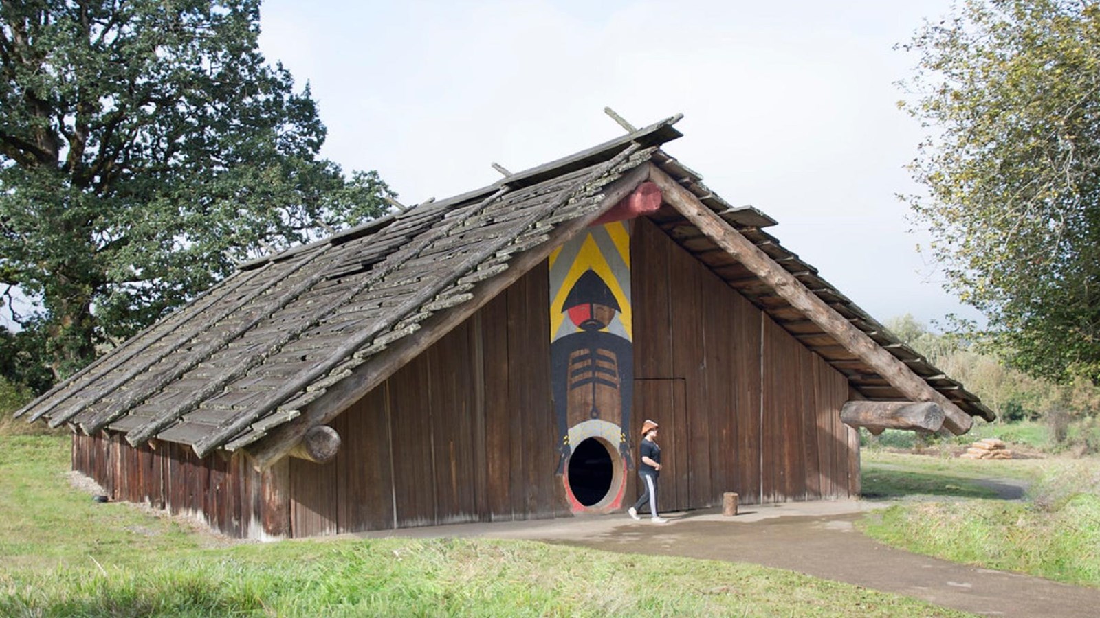 A low building made of cedar planks with a small round door sits in a field of green grass
