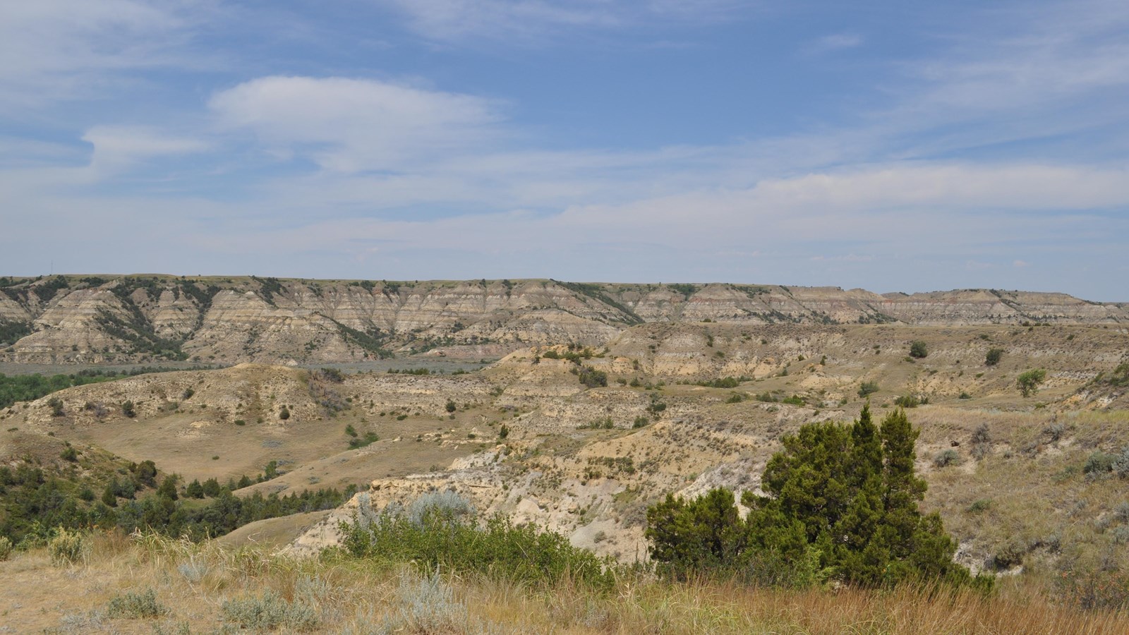 A view across a valley in Theodore Roosevelt National Park, under a blue sky.