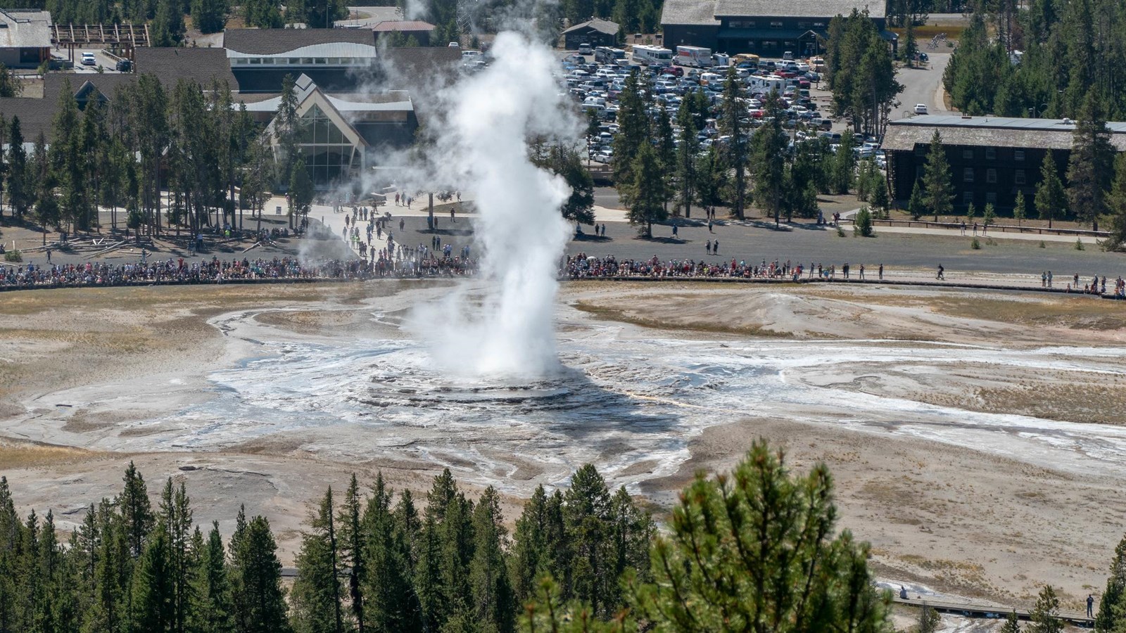Water and steam erupt out of a geyser while people watch.