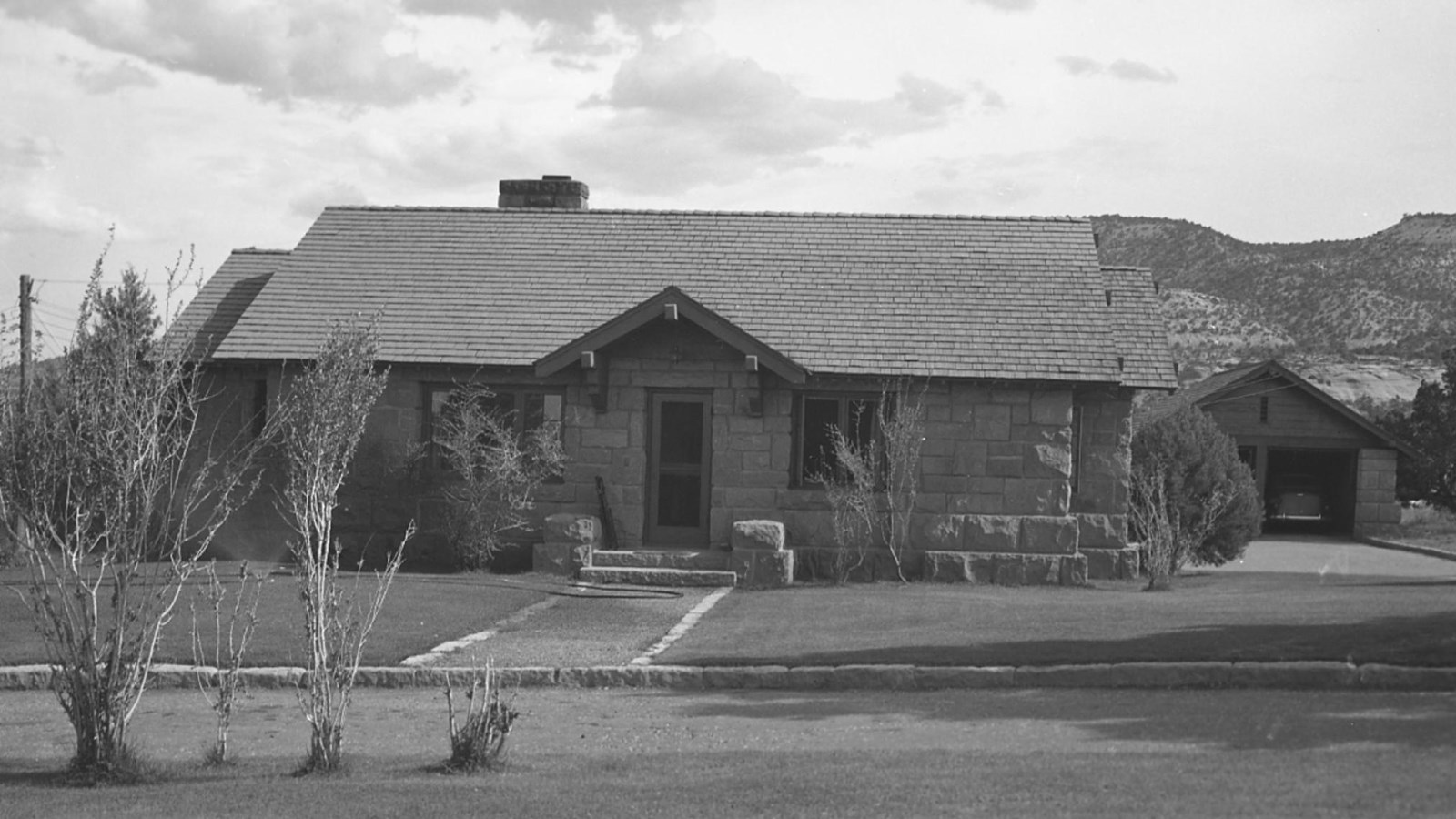 One story house and separate garage made of large stone blocks. Wood shingle roofs.