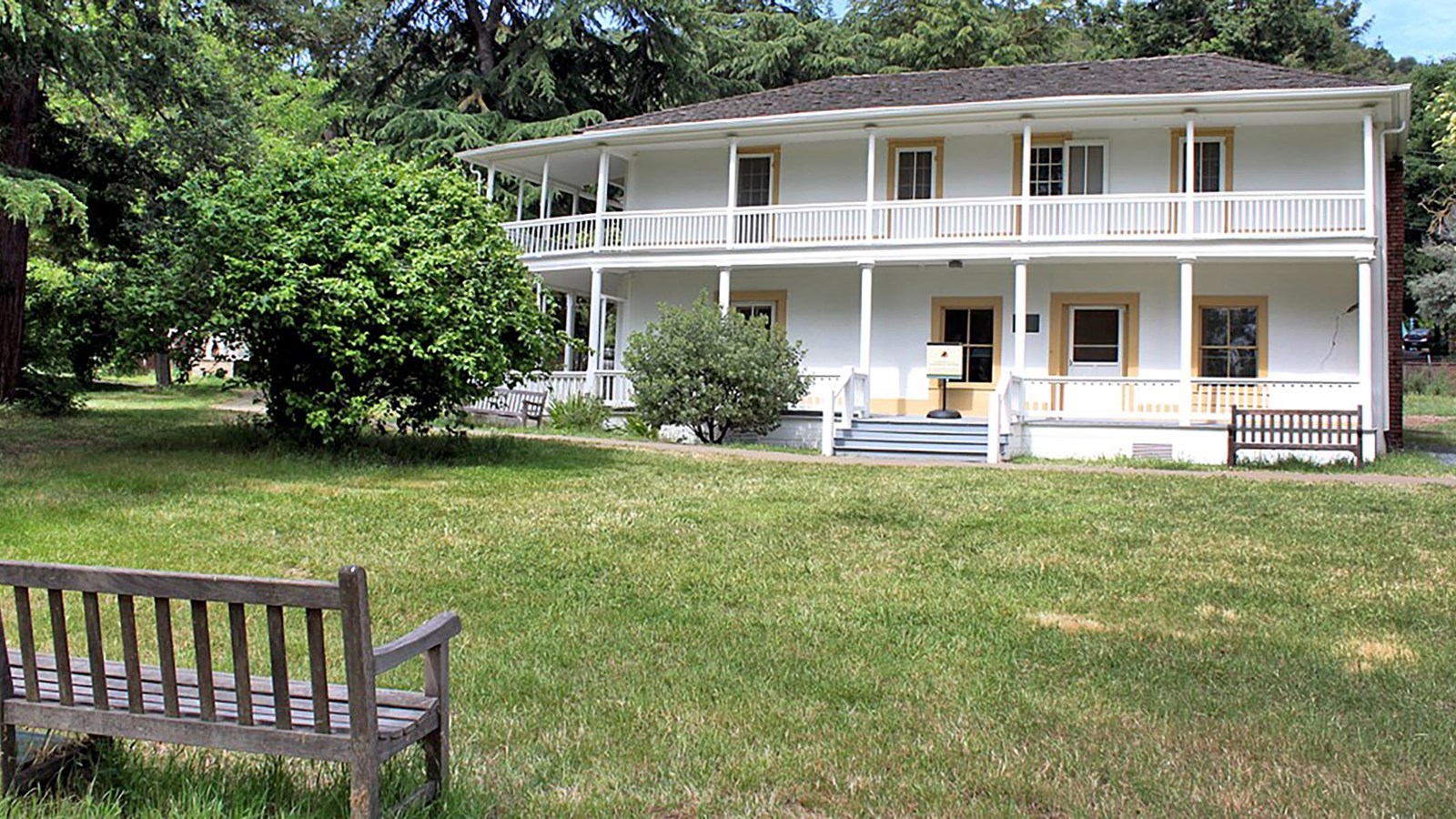 A two story home with end-to-end porches on both levels. A park bench sits in the foreground. 