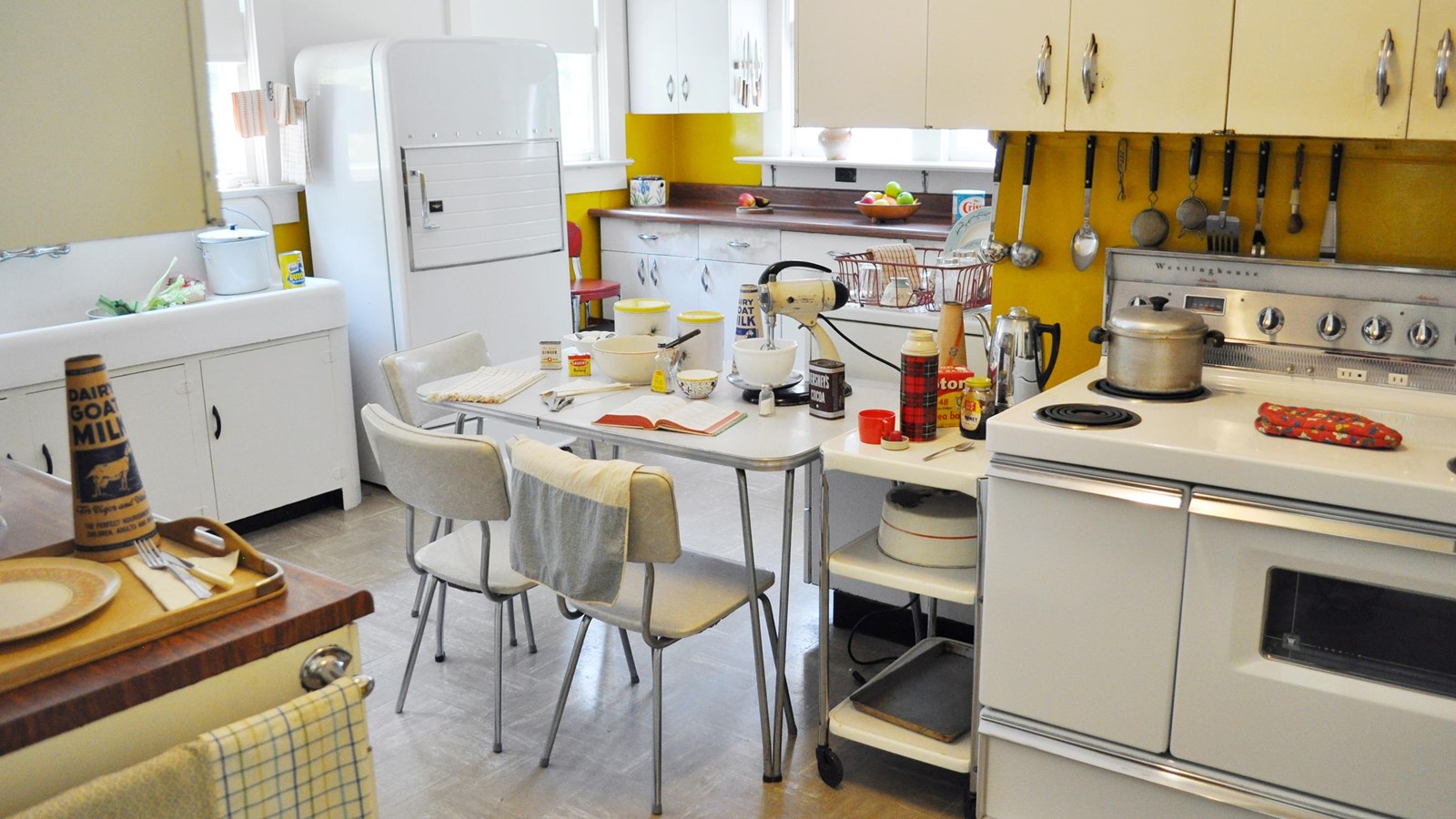 image of kitchen with yellow walls, white cabinets, and bowls, recipe books and appliances laid out