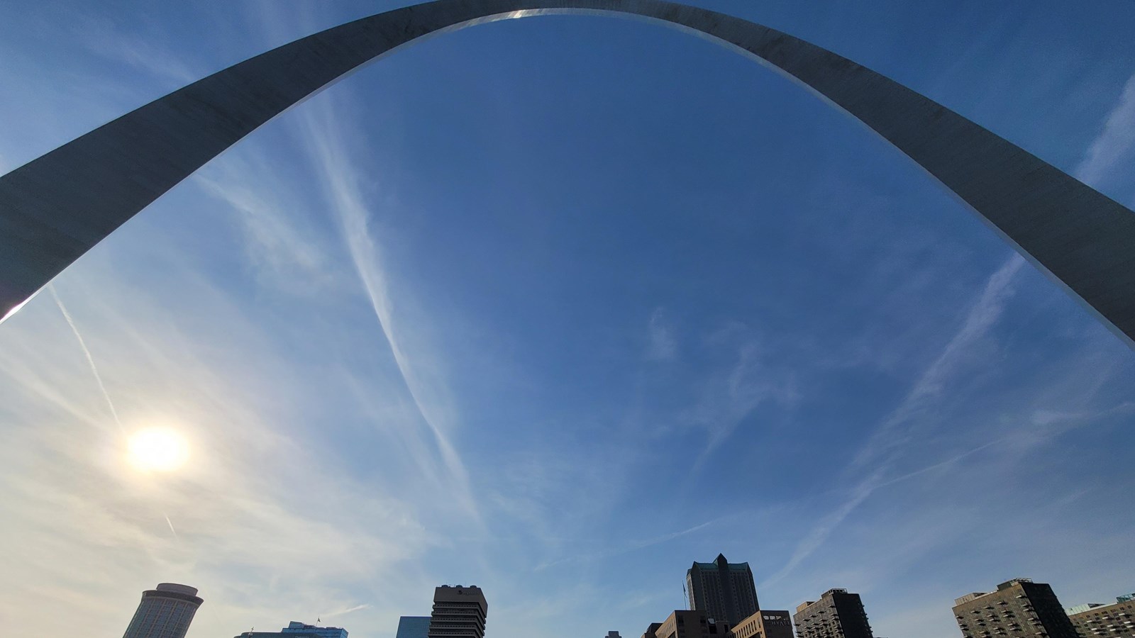 the arch curving overhead against a blue sky, city buildings behind