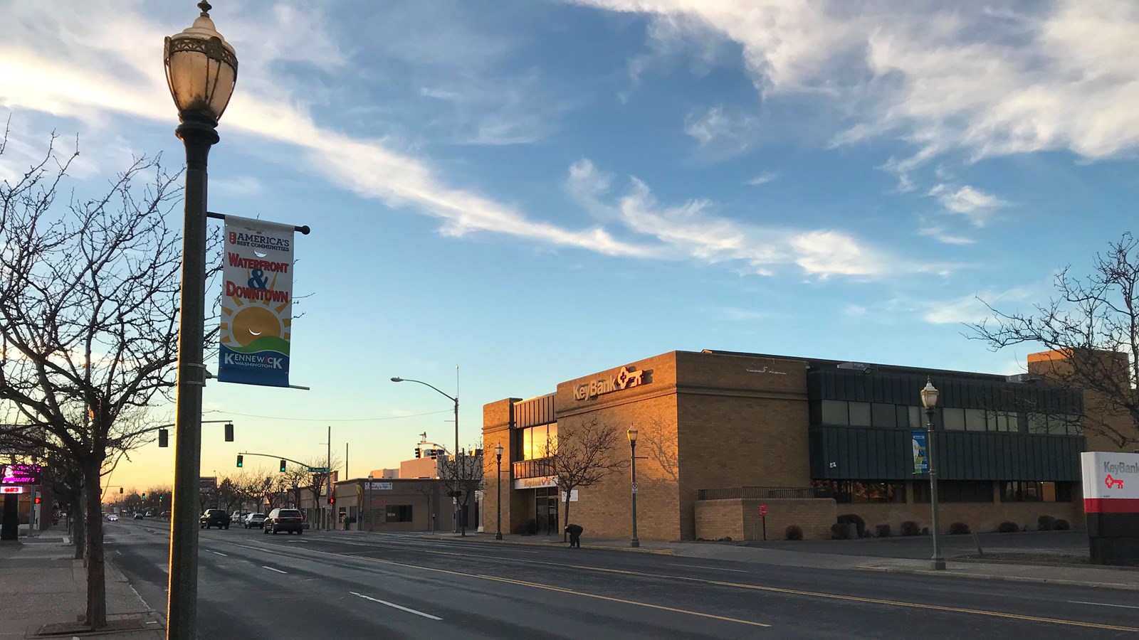 A color photo of a lamppost on the left side of a road with a building on the right side. 