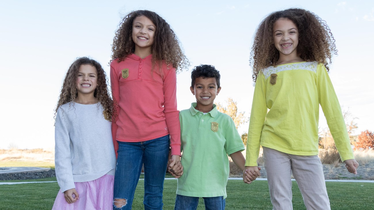 Four kids in bright colored clothes stand in a grassy field.
