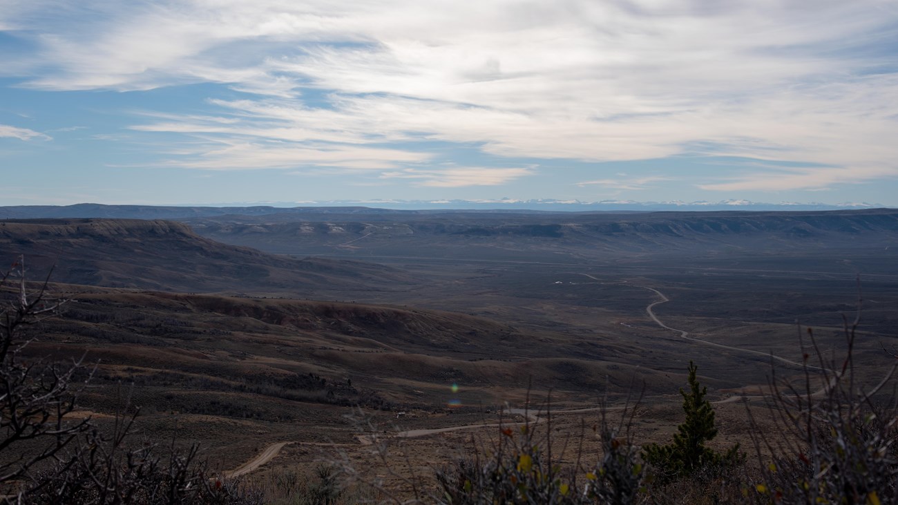 A road travels away through the valley with ridges and snow-capped mountains in the distance