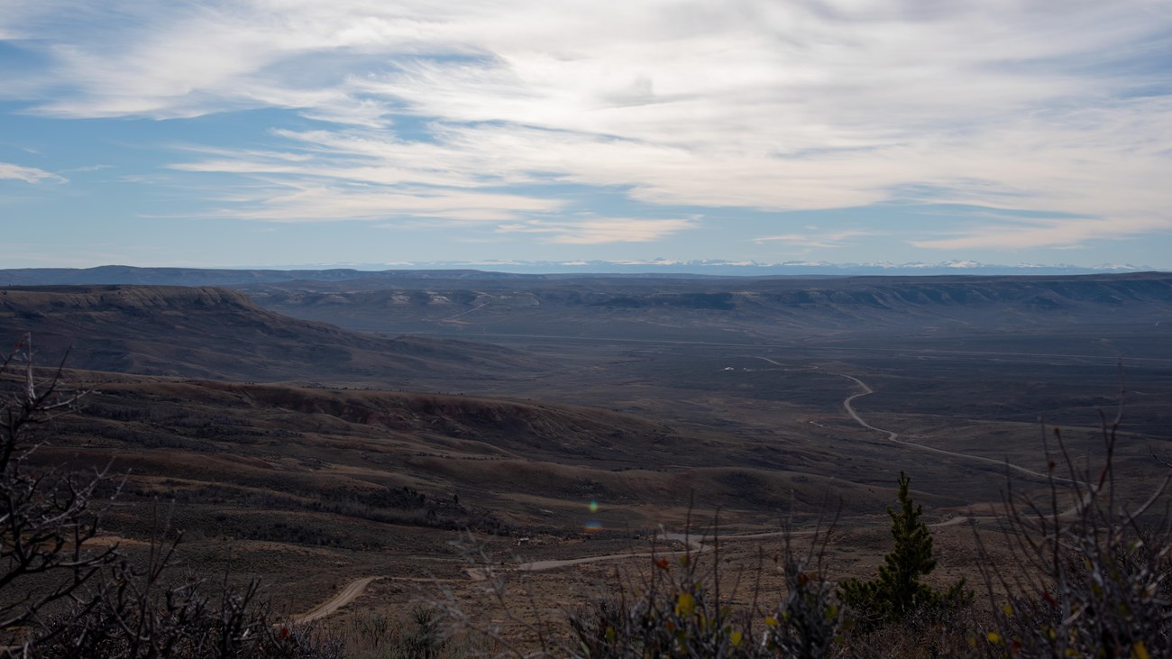 A road travels away through the valley with ridges and snow-capped mountains in the distance