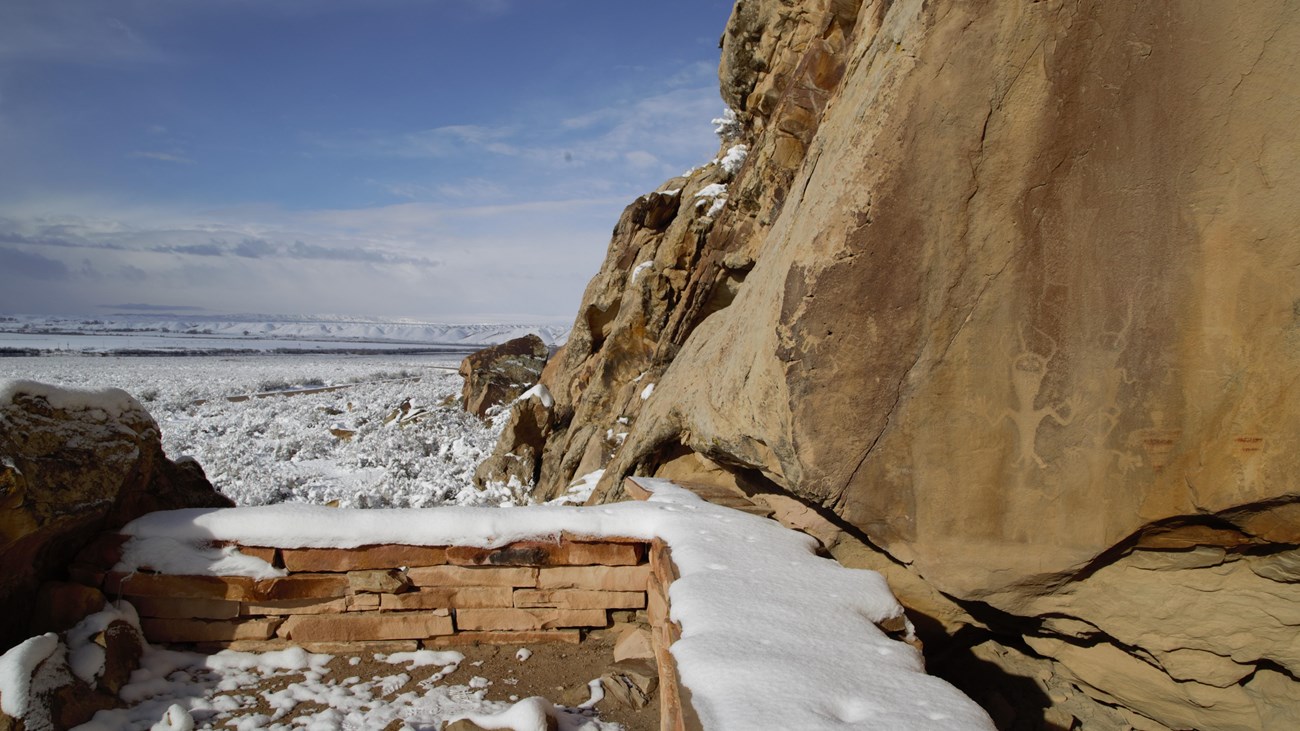 A short stone wall covered in snow offers a place to view petroglyphs and pictographs.
