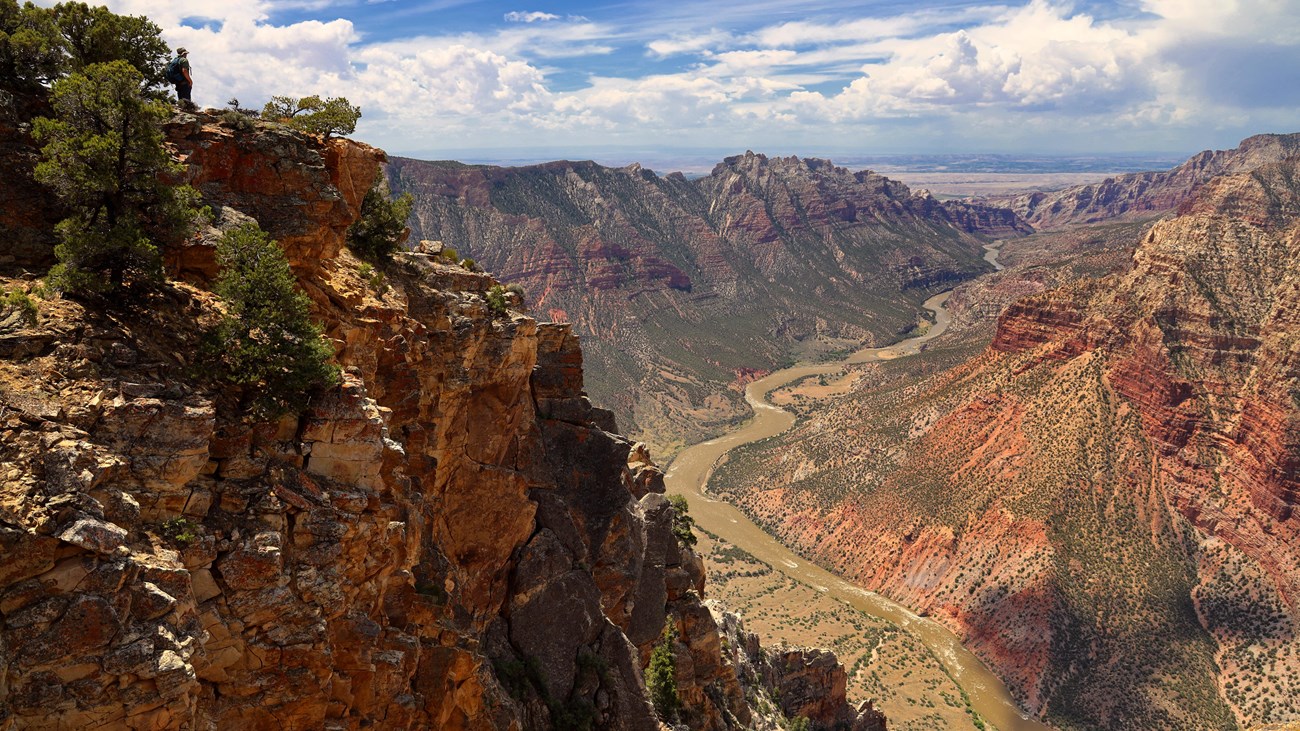 Large walls of orange red rock rise as a river flows through a deep canyon. 