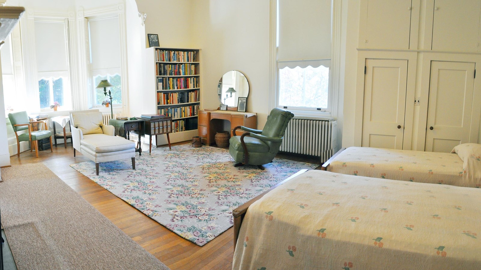 image of bedroom with twin beds, chairs, bookshelves and a large bay window