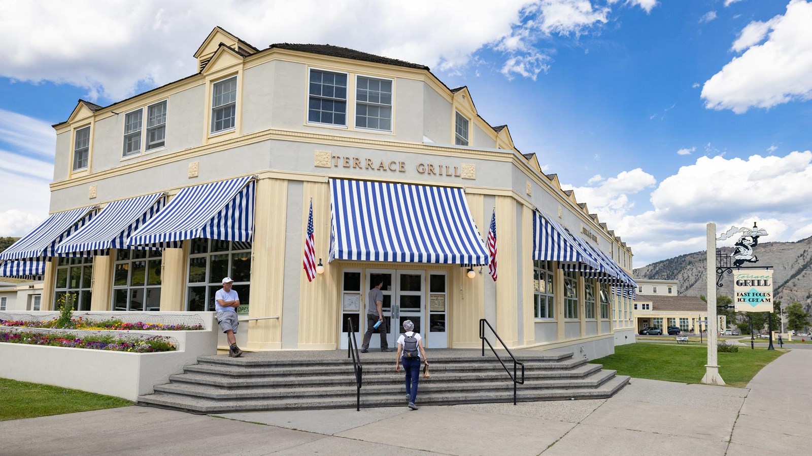 An off-white colored concrete building with pale yellow trim and striped blue and white awnings.