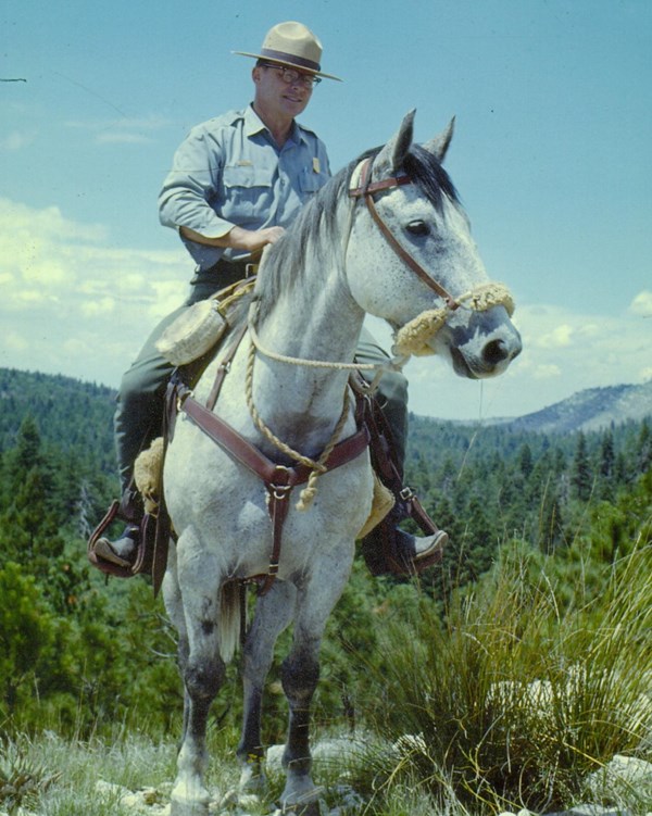 A uniformed park ranger sits astride a horse. 